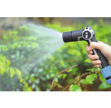 Eine Hand hält eine Gartenspritze und bewässert Pflanzen.