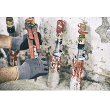 Eine Hand mit Arbeitshandschuh hält eine Rohrzange an einem Wasserhahn.