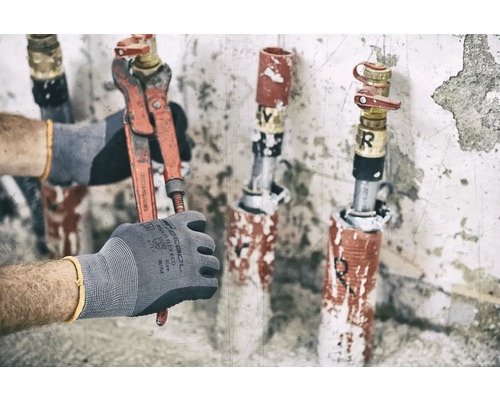 Eine Hand mit Arbeitshandschuh hält eine Rohrzange an einem Wasserhahn.