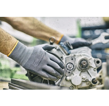 Person mit Montagehandschuhen repariert einen Motorblock mit einem Schraubenschlüssel