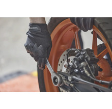 Eine Person mit Handschuhen benutzt einen Schraubenschlüssel an einem Motorrad.