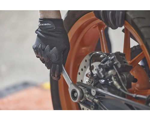 Eine Person mit Handschuhen benutzt einen Schraubenschlüssel an einem Motorrad.