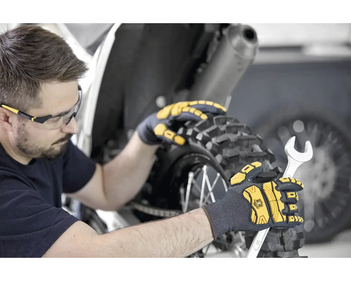 Mann mit Schutzbrille und Arbeitshandschuhen, der mit einem Schraubenschlüssel an einem Motorrad arbeitet