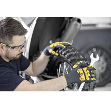 Mann mit Schutzbrille und Arbeitshandschuhen, der mit einem Schraubenschlüssel an einem Motorrad arbeitet