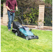 Eine Person verwendet einen batteriebetriebenen Rasenmäher von Makita auf einer gepflegten Rasenfläche vor einem Gartenzaun mit Steinmauer.