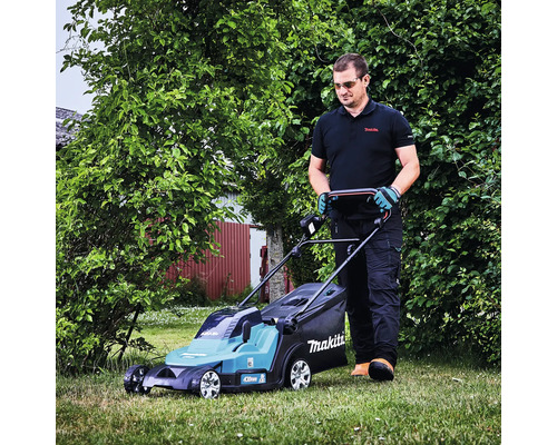 Ein Mann mäht den Rasen in einem Garten mit einem Makita Akku-Rasenmäher.