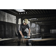 Bauarbeiter mit Helm und Gehörschutz schneidet mit einem Makita Winkelschleifer Metall auf einer Baustelle, Funkenflug.