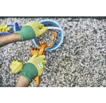 Hände mit Gartenhandschuhen befüllen einen Eimer mit einer Schaufel und Steinen, umgeben von Spielzeug für den Sandkasten.
