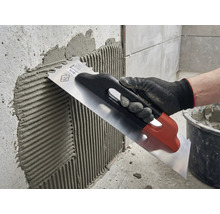 Aufbringen von Fliesenkleber mit einer rostfreien Stahltraufel auf eine Wand