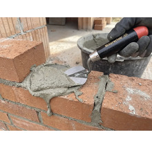 Eine Hand mit Handschuh trägt mit einer Maurerkelle Mörtel auf eine Ziegelmauer auf