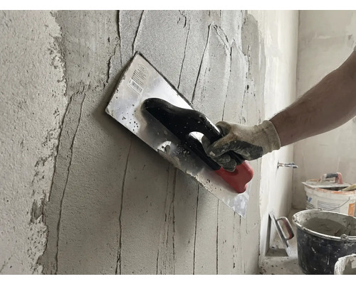 Handwerker trägt Putz mit einer Glättkelle auf eine Wand auf.