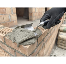 Maurerhand mit Kelle beim Auftragen von Mörtel auf Ziegel