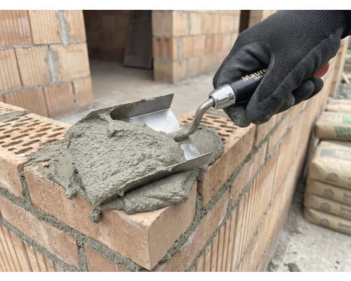 Maurerhand mit Kelle beim Auftragen von Mörtel auf Ziegel