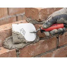 Ein Maurer legt mit einer Maurerkelle Mörtel auf Ziegelsteine.