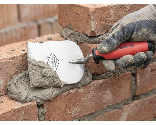 Ein Maurer legt mit einer Maurerkelle Mörtel auf Ziegelsteine.