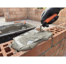 Maurer legt mit einer Maurerkelle Mörtel auf eine Mauer.