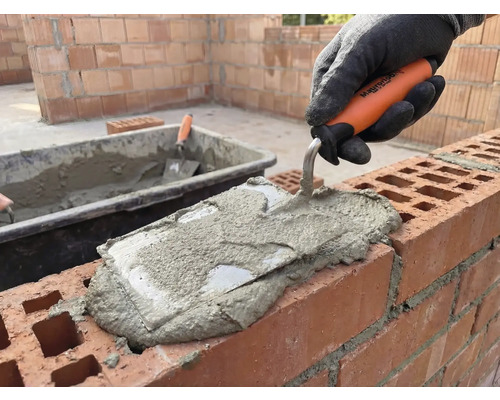 Maurer legt mit einer Maurerkelle Mörtel auf eine Mauer.