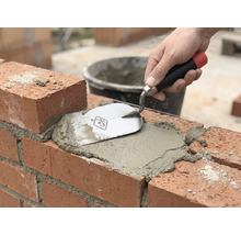 Maurerhandwerk: Ziegelstein wird mit Mörtel und einer Maurerkelle verfugt.