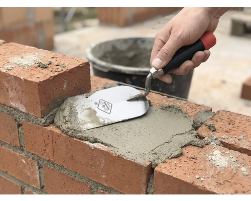 Maurerhandwerk: Ziegelstein wird mit Mörtel und einer Maurerkelle verfugt.