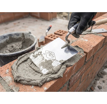 Maurer bei der Arbeit mit Maurerkelle, Mörtel und Ziegeln