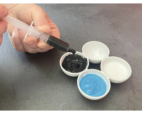 Hand füllt mit Spritze schwarze Farbe in einen Farbmischteller