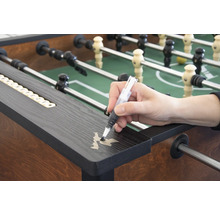 Eine Person retuschiert Kratzer auf einem Tischfußballtisch mit einem Lackstift.