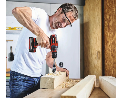 Mann bohrt mit einem Akku-Bohrschrauber ein Loch in ein Holzstück