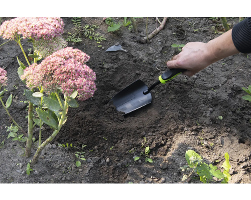 Gartenszene mit Hand, die eine Pflanzschaufel in die Erde steckt