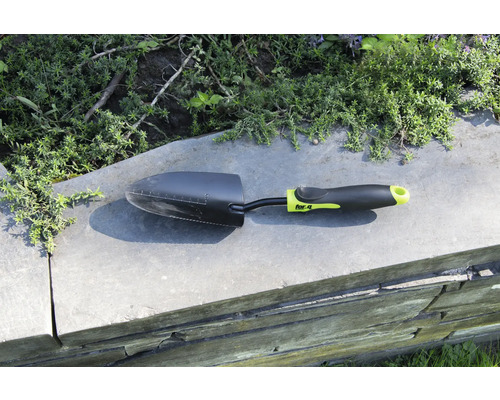 Gartenschaufel auf einer Mauer mit Pflanzen im Hintergrund