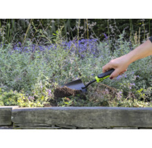 Eine Person verwendet eine kleine Gartenschaufel, um in einem Blumenbeet zu graben.