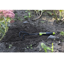 Gartenharke im Erdreich neben einer Blume