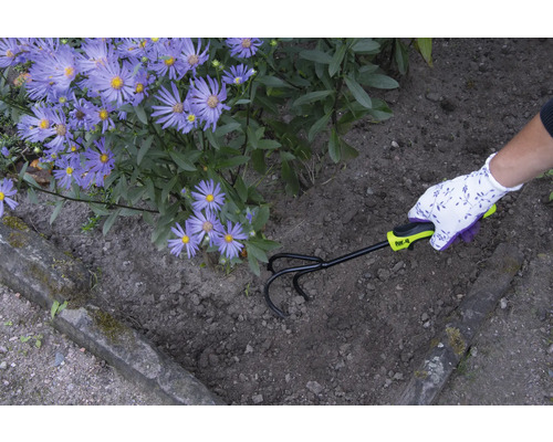 Gartenarbeiter lockert Erde mit einem Kultivator neben lila Blumen auf.