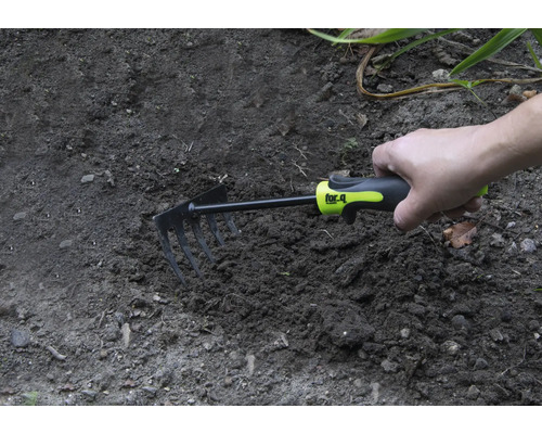 Hand hält eine kleine Harke im Gartenboden