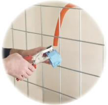 Hände befestigen ein Wellrohr mit einer Montagezange an einer Schalterdose vor einem Metallgitter.