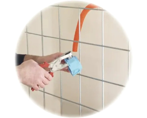 Hände befestigen ein Wellrohr mit einer Montagezange an einer Schalterdose vor einem Metallgitter.