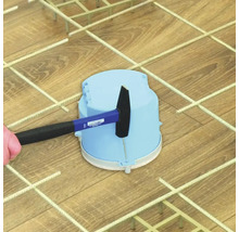Ein Hammer schlägt auf eine blaue Elektroinstallationsdose aus Kunststoff auf einem Metallgitter.