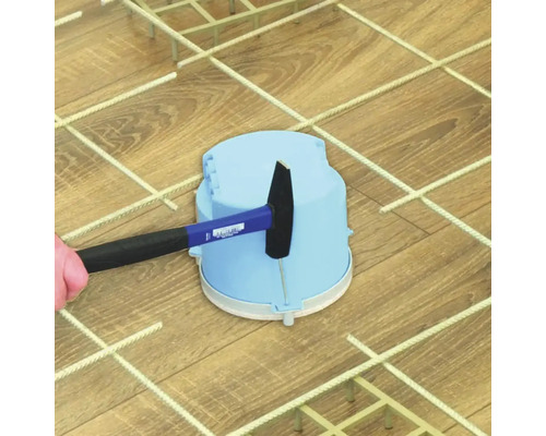 Ein Hammer schlägt auf eine blaue Elektroinstallationsdose aus Kunststoff auf einem Metallgitter.