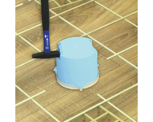 Ein Hammer klopft eine blaue Elektro-Betonbaudose auf einem Bewehrungsgitter für Betonarbeiten fest.