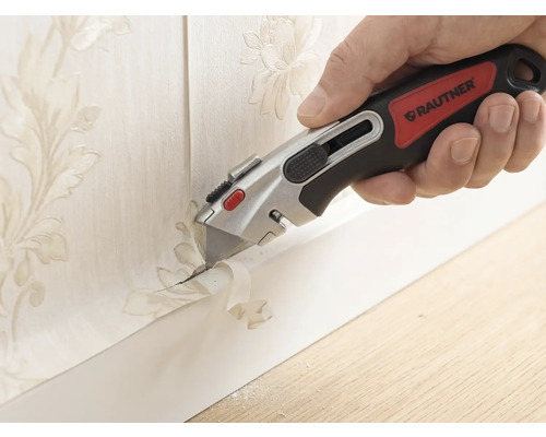 Hand mit Rautner Cuttermesser beim präzisen Abschneiden von Tapete mit Blumenmuster an einer Fußleiste.