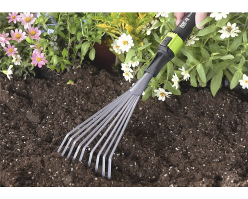 Handgeführter kleiner Fächerbesen von for_q wird in dunkler Blumenerde neben rosa und weißen Blumen verwendet.