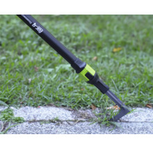 Fugenkratzer for_q fitconnect entfernt Unkraut aus einer Pflasterfuge auf einer Gehwegplatte neben einer Rasenfläche.