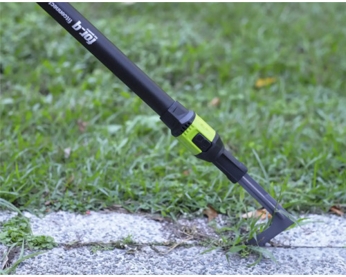 Fugenkratzer for_q fitconnect entfernt Unkraut aus einer Pflasterfuge auf einer Gehwegplatte neben einer Rasenfläche.