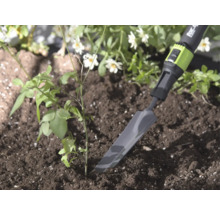 Schmale Pflanzkelle aus Metall von for_q in der Erde neben einer kleinen Pflanze, helle und natürliche Gartenumgebung.