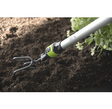 Gartenkralle mit Stiel lockert Erde neben Pflanzen auf.