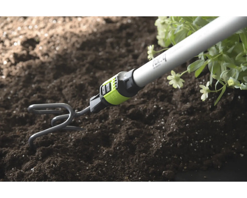 Gartenkralle mit Stiel lockert Erde neben Pflanzen auf.