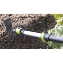 Handhacke mit Metallblatt und drei Zinken in dunkler Gartenerde neben Blumen.