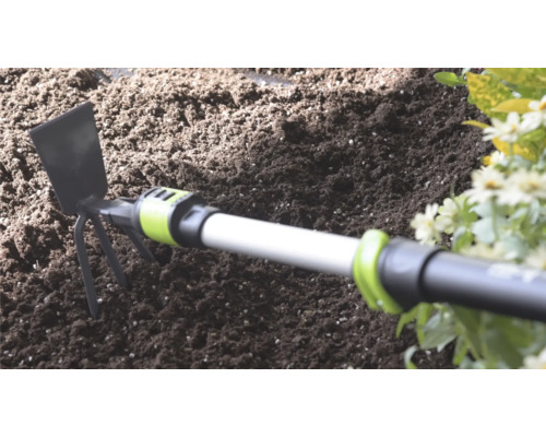 Handhacke mit Metallblatt und drei Zinken in dunkler Gartenerde neben Blumen.