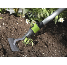 Garten-Pendelhacke mit grauer Klinge und grünem Anschlussstück bei der Unkrautentfernung in dunkler Erde neben einer Pflanze.