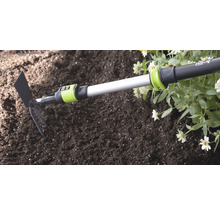 for_q Kombigerät aus Kleingrubber und Häufelplatte mit Teleskopstiel bei der Gartenarbeit in Erde neben Blumen.