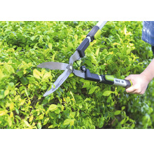 Manuelle for_q Heckenschere beim Schneiden einer grünen Hecke im Garten.